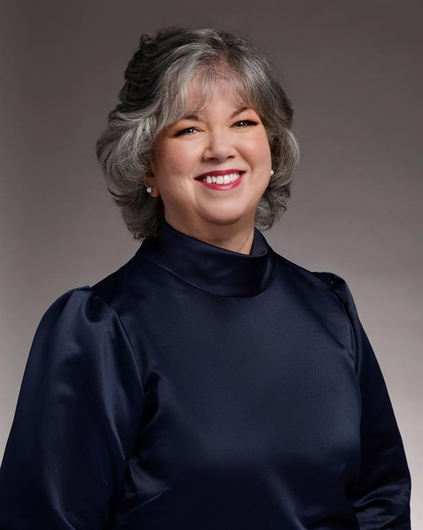 Lorin MacDonald smiles for a professional headshot. She is wearing a royal blue, satin shirt with puffy sleeves and is in front of a dark grey background.